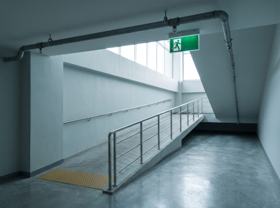 Rampa de acessibilidade com corrimão duplo e piso tátil, com porta corta-fogo ao fundo